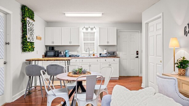 A compact kitchen with white cabinets, a dining area with a round table and chairs, and a cozy seating area with a white sofa. - Bee Happy Sparta Mountain Cottage (Sparta)