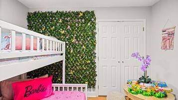 Habitación infantil con literas, un muro decorativo, una puerta y una mesita llena de juguetes.