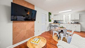 A modern living room with a flat-screen TV, a wooden accent wall, a dining area with a table and chairs, and a kitchen with white cabinets. - Bee Happy Sparta Mountain Cottage (Sparta)