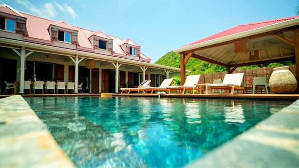 A pool area with lounge chairs and a covered seating area, surrounded by a building with a red roof.
