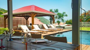 A poolside area with lounge chairs, a covered seating area, and a dining table set for a meal.