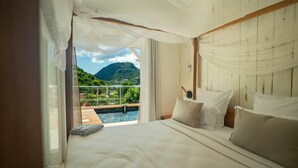 A bedroom with a large bed, white curtains, and a view of a pool and mountains.