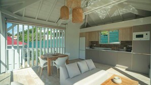 A modern kitchen with a refrigerator, microwave, and wooden cabinets. There is a dining area with a table and chairs, and a sofa.
