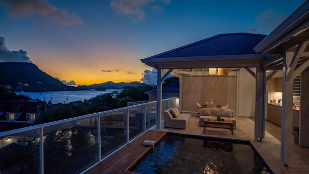 A modern outdoor pool area with a view of the sea and mountains at dusk.