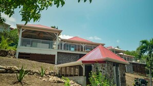 Un immeuble à plusieurs étages, avec un toit rouge, un balcon et une structure en pierre au premier plan.