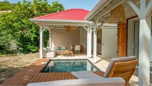 Un espace piscine doté d’une terrasse en bois, de chaises longues, d’un coin salon abrité et d’un bâtiment au toit rouge.