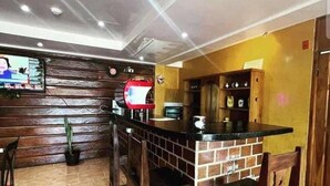 Zona de bar amb un mostrador de maó, cadires de fusta i una pantalla de televisió que mostra un menú.