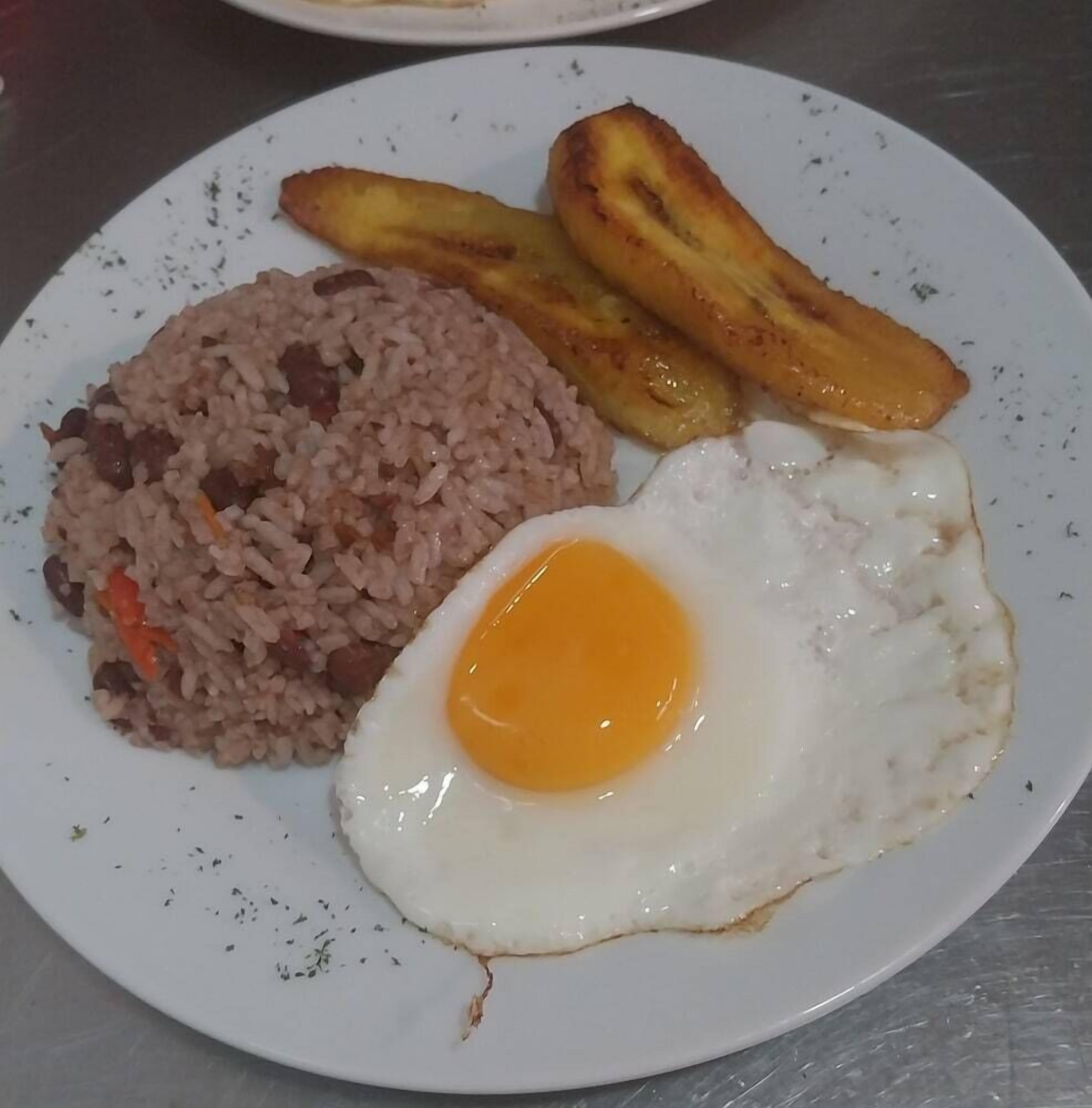 Un plato de arroz frito, un huevo frito y dos tajadas de plátano frito.