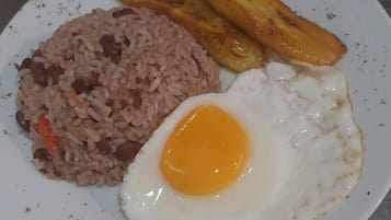 Un plato de arroz frito, un huevo frito y dos tajadas de plátano frito.