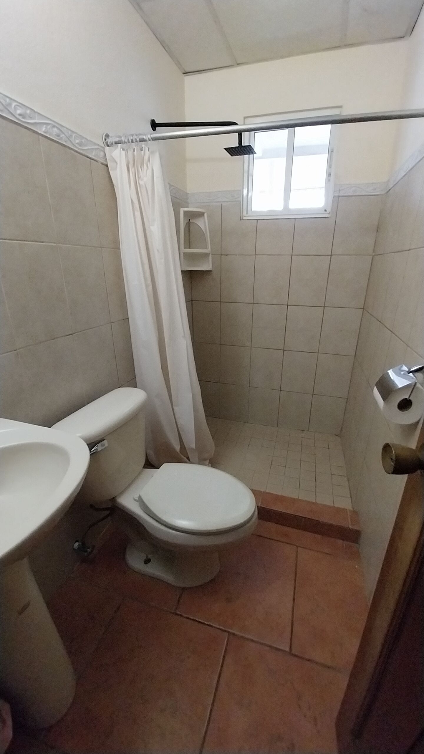 Un baño con inodoro, lavamanos, ducha y ventana.
