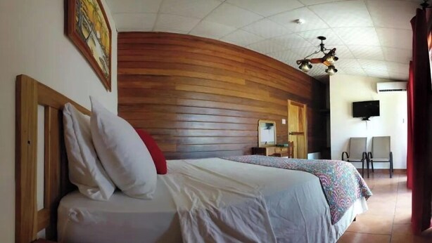 Habitació d'hotel amb dos llits, panells de fusta a les parets, ventilador de sostre, televisió i escriptori amb cadira.