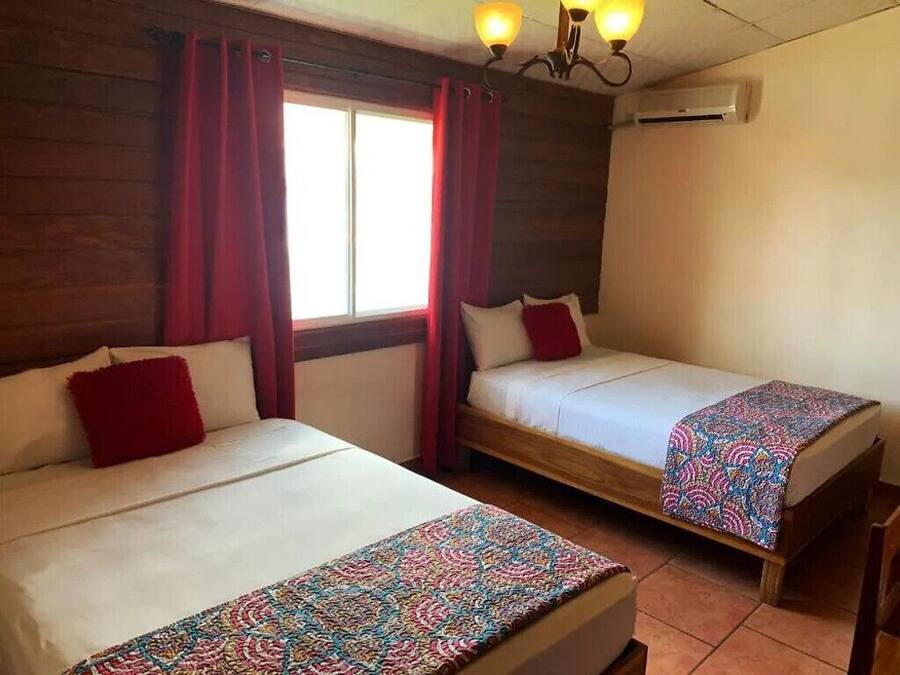Una habitación con dos camas, cada una con una colcha estampada, cortinas rojas y un aplique de techo.