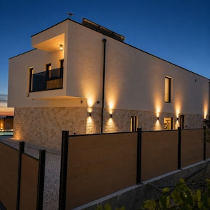 Un bâtiment moderne à deux étages, doté d’un toit plat, d’une piscine et d’une entrée sécurisée par un portail.
