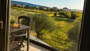 Un balcón con mesa y sillas, con vistas a un paisaje verde con casas y un cielo despejado.