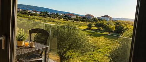 A balcony with a table and chairs, overlooking a green landscape with houses and a clear sky.