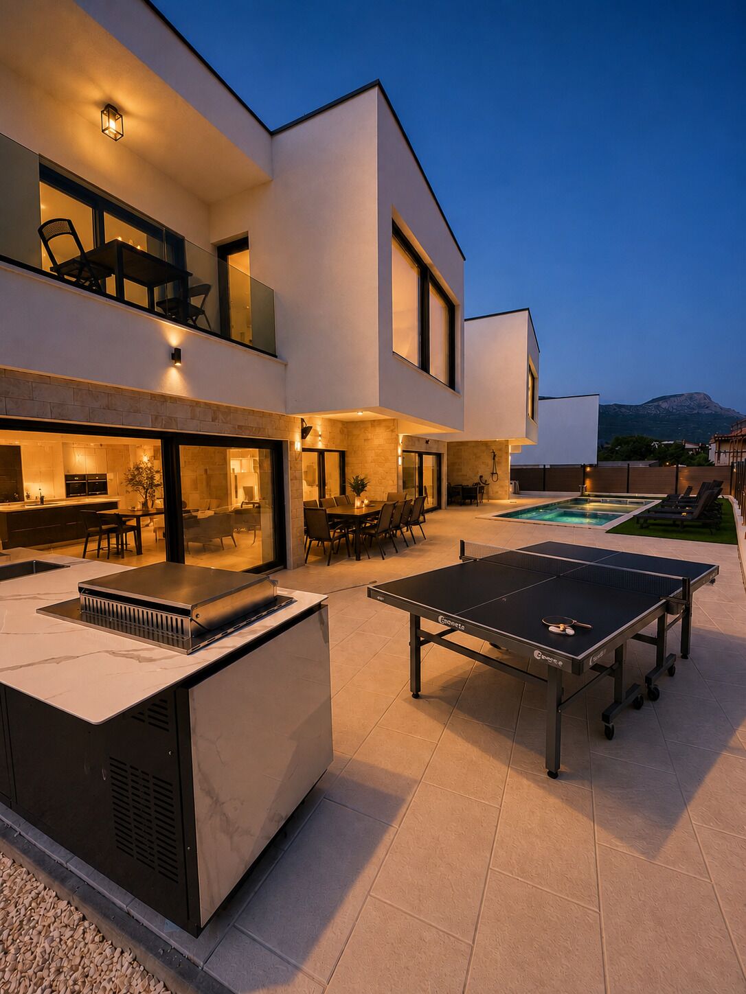 A modern outdoor living area with a pool, a ping pong table, and a barbecue grill.