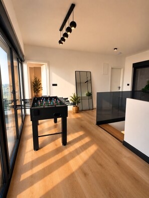 Un intérieur moderne avec un baby-foot, un grand miroir et une vue à travers une porte vitrée.