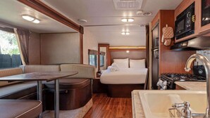 Een compact RV-interieur met een kitchenette, een bed, een eethoek en een kleine badkamer.