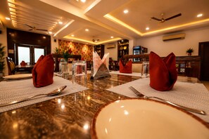 A dining table set with red napkins, clear glassware, and a decorative centerpiece. - The Elegance Resort (Chittorgarh)