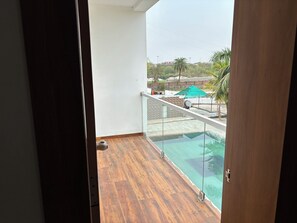 A balcony with a wooden floor and a glass railing overlooking a swimming pool. - The Elegance Resort (Chittorgarh)