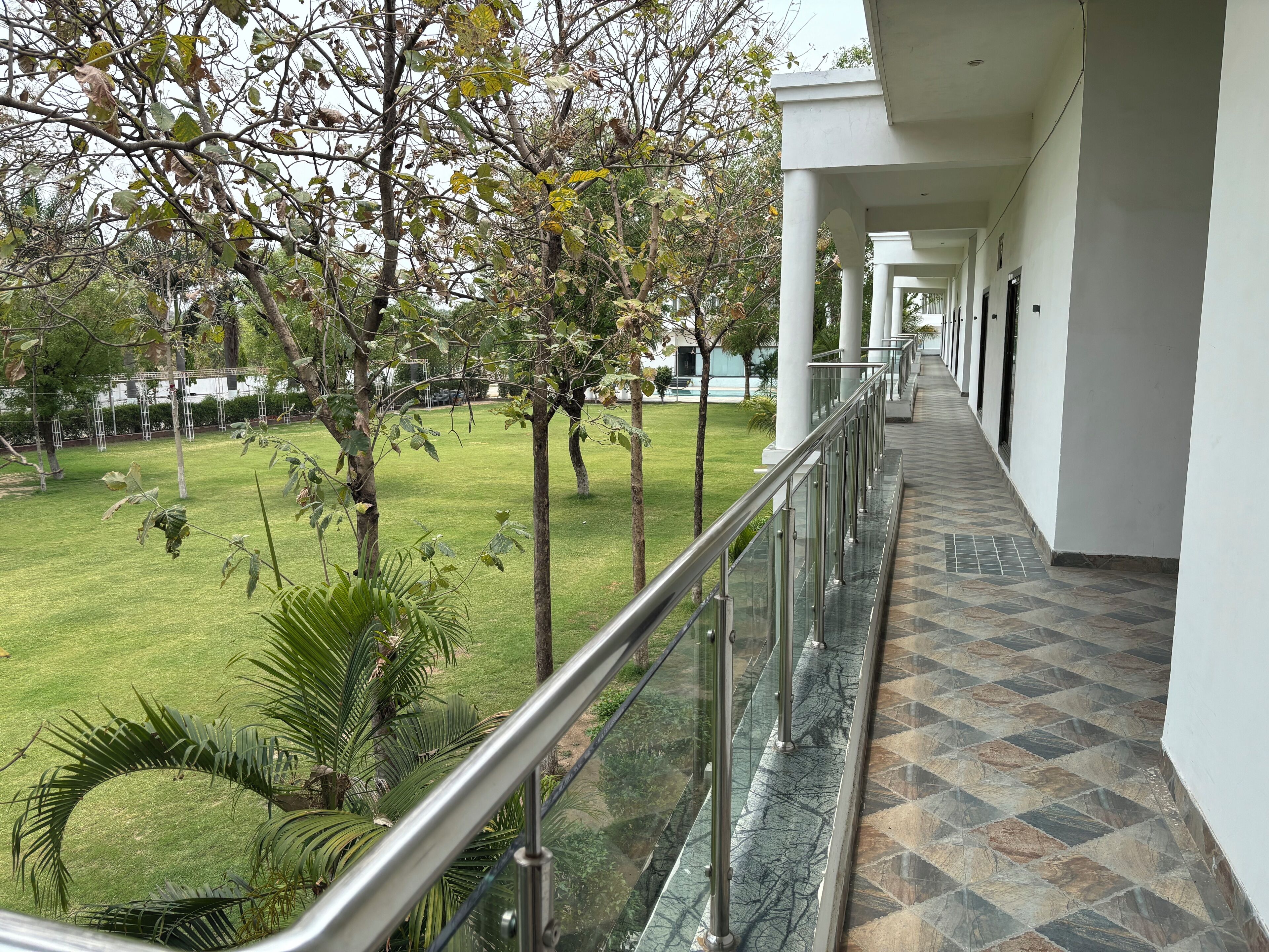A corridor with a glass railing, leading to a grassy area with trees and a building in the background.
