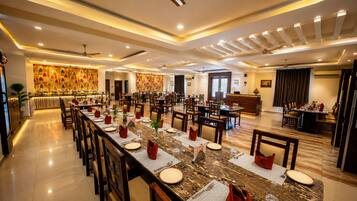 A spacious hotel dining area with multiple tables and chairs, a reception desk, and a decorative wall.
