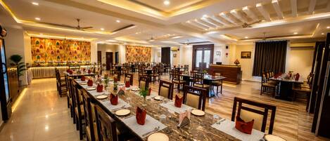 A spacious hotel dining area with multiple tables and chairs, a reception desk, and a decorative wall.