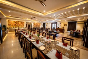 Amplia sala de comedor de hotel con varias mesas y sillas, un mostrador de recepción y una pared decorativa.