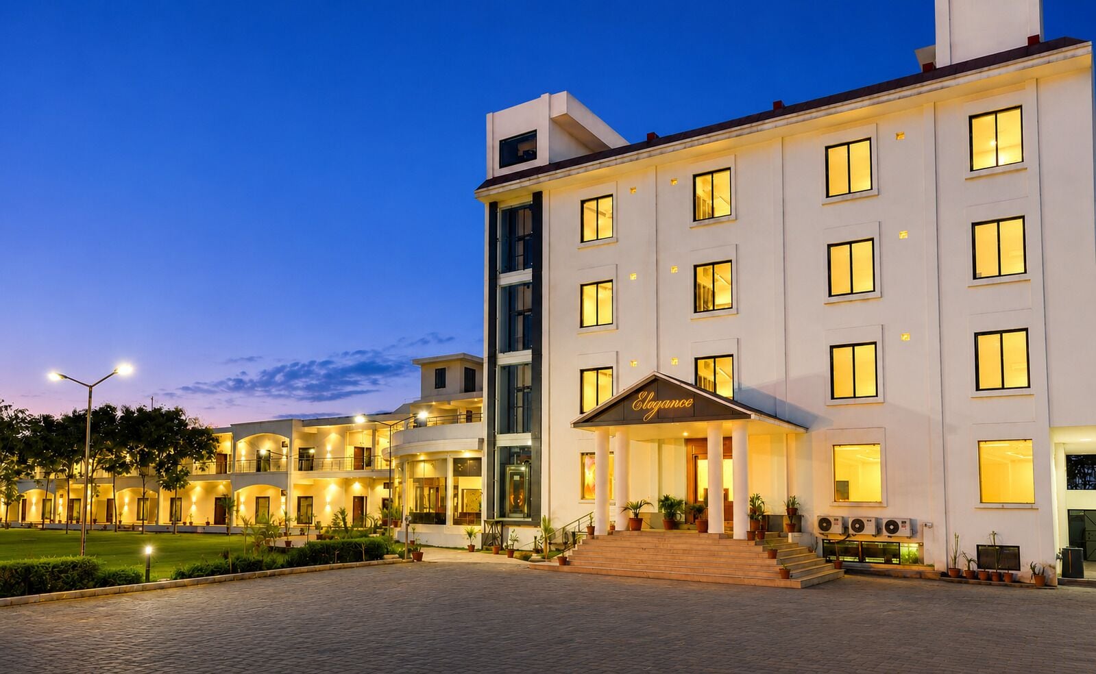 Un hotel de varios pisos con una entrada bien iluminada y un patio ajardinado.