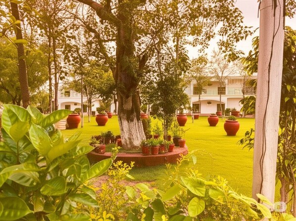 A courtyard with a large tree, potted plants, and a building in the background. - The Elegance Resort (Chittorgarh)