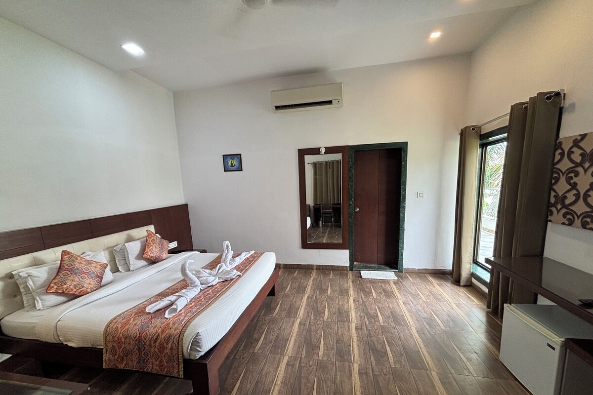 Habitación de hotel con una cama grande, piso de madera, un escritorio pequeño y una ventana con cortinas.