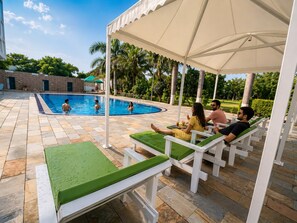 A swimming pool area with lounge chairs and a covered seating area. - The Elegance Resort (Chittorgarh)