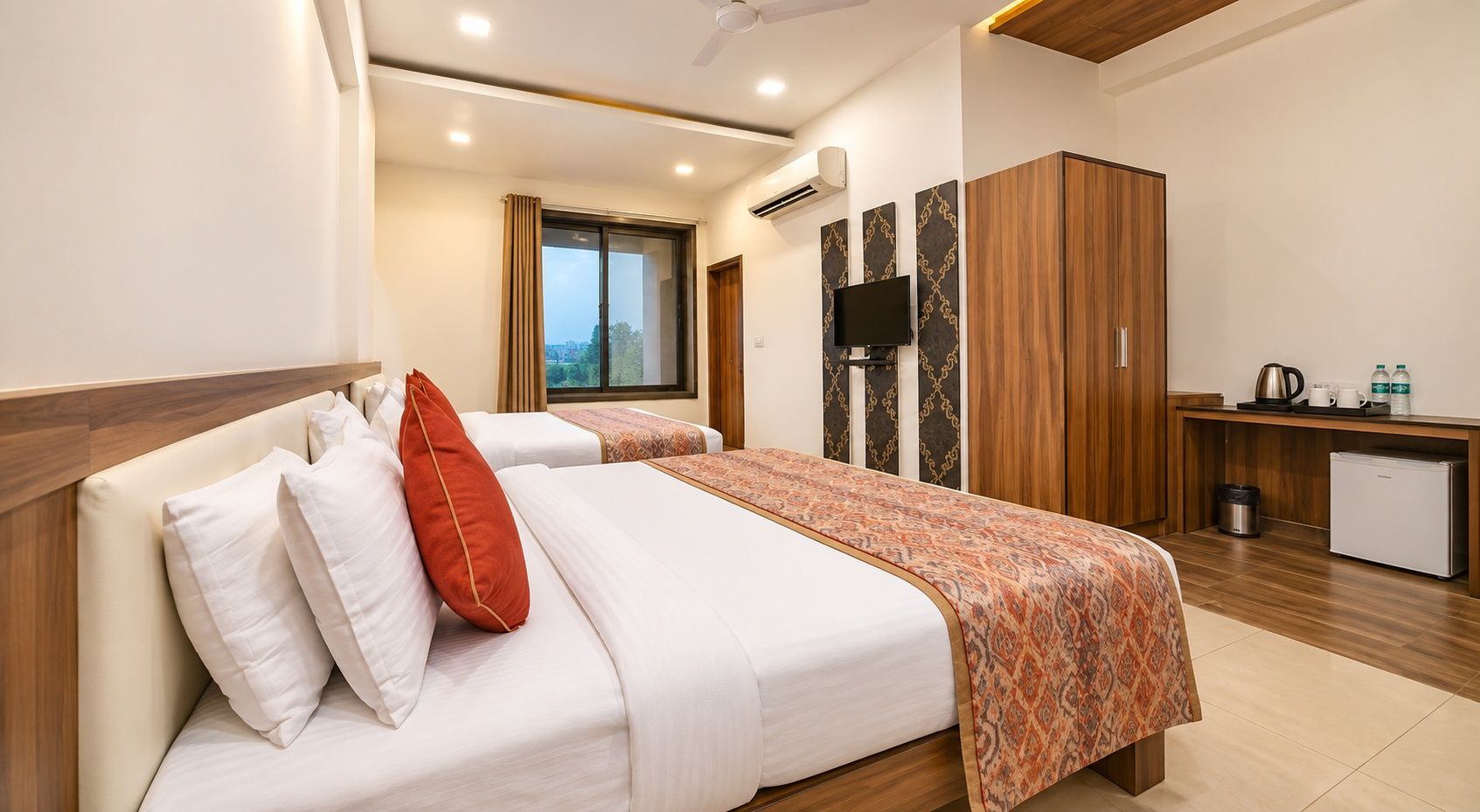 A hotel room with two beds, a TV, a wardrobe, and a kitchenette.