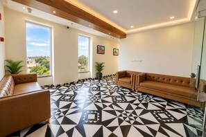 A lobby with a geometric patterned floor, leather sofas, large windows, and indoor plants. - The Elegance Resort (Chittorgarh)