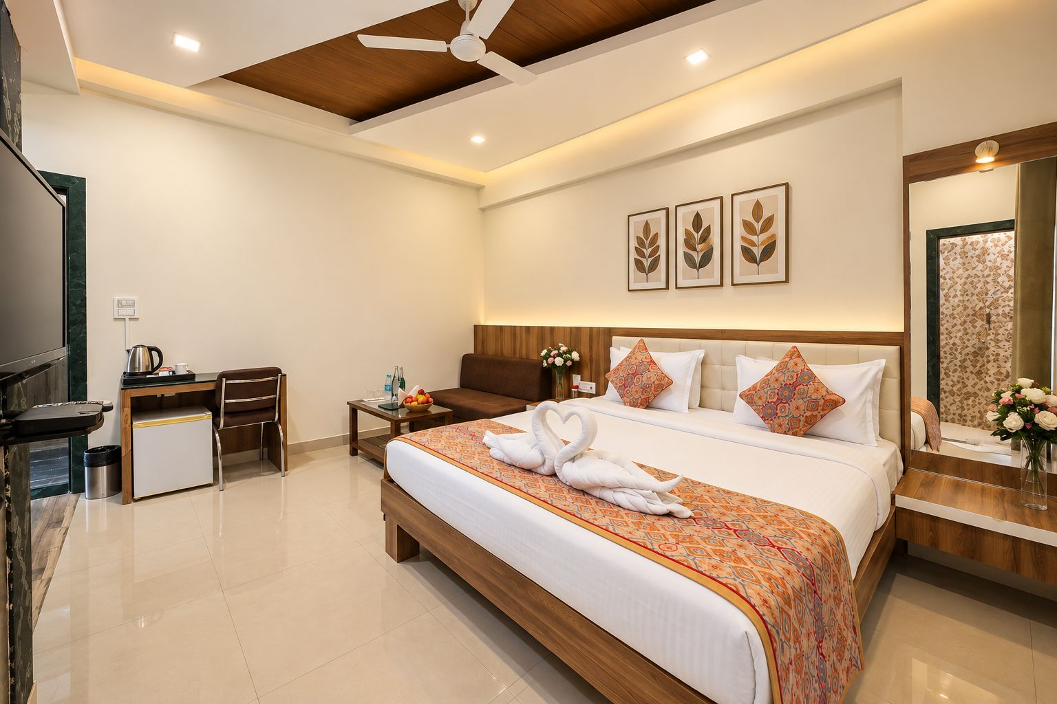 A hotel room with a large bed, a desk with a chair, a small refrigerator, a ceiling fan, and a mirror with a floral pattern.