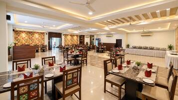 A spacious dining area with multiple tables and chairs, ceiling fans, and a buffet setup.