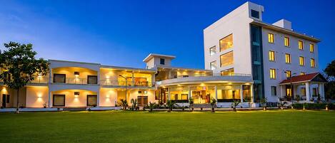 A multi-story hotel with a well-lit entrance and a grassy lawn in front.