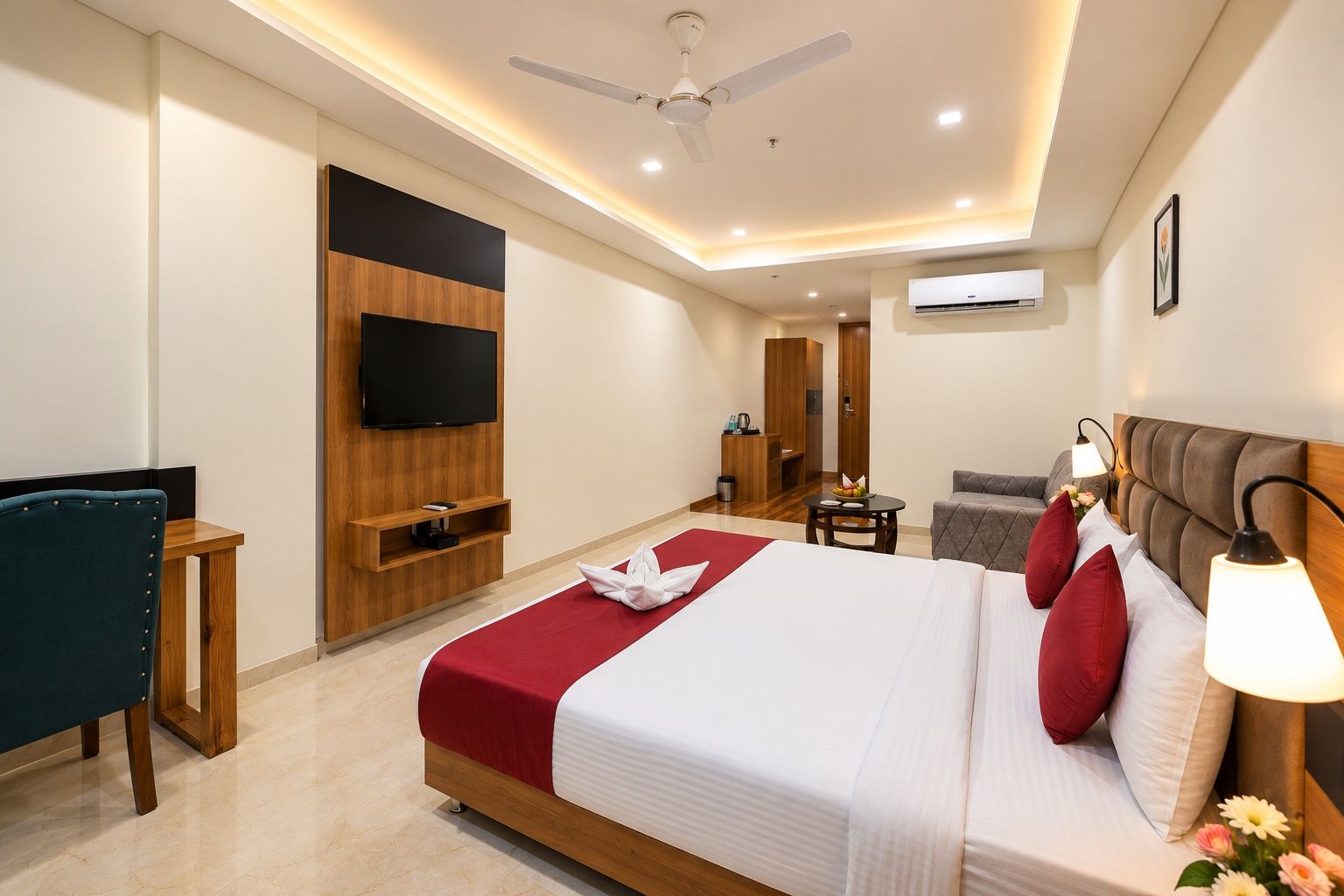 A hotel room with a bed, a television, a ceiling fan, a small table with a fruit bowl, and a sofa.