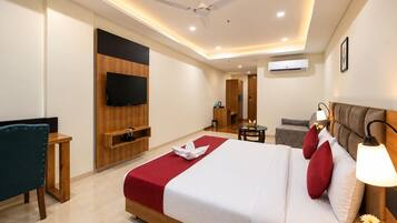 A hotel room with a bed, a television, a ceiling fan, a small table with a fruit bowl, and a sofa.