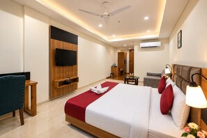 Habitación de hotel con cama, televisor, ventilador de techo, una pequeña mesa con frutero y un sofá.