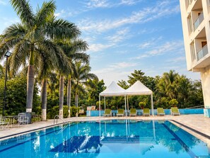 A swimming pool with lounge chairs and a gazebo, surrounded by palm trees and a clear sky. - The Elegance Resort (Chittorgarh)