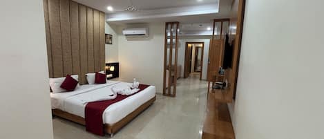 Habitación de hotel con una cama grande, un cabecero de madera, un televisor de pantalla plana y una nevera pequeña.