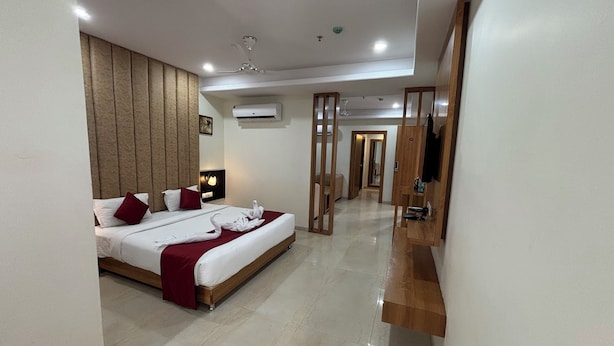 A hotel room with a large bed, a wooden headboard, a flat-screen TV, and a minibar. - The Elegance Resort (Chittorgarh)