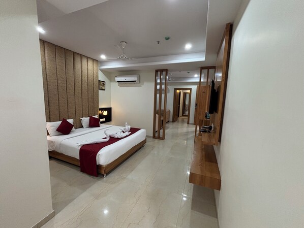 A hotel room with a large bed, a wooden headboard, a flat-screen TV, and a minibar. - The Elegance Resort (Chittorgarh)