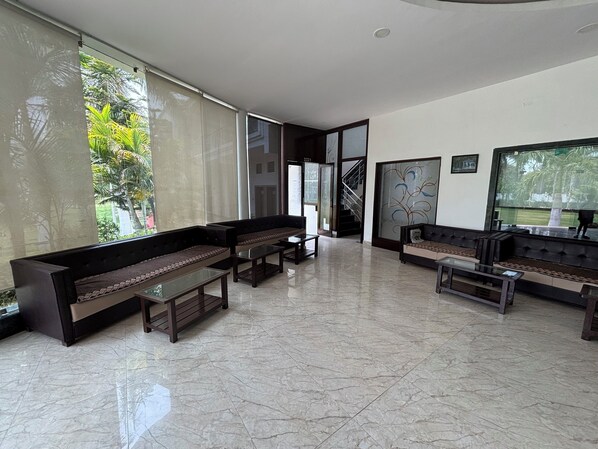 Un hall d’entrée spacieux, doté de canapés sombres et de tables en verre, de grandes fenêtres offrant une vue sur la verdure et d’un aménagement intérieur moderne.