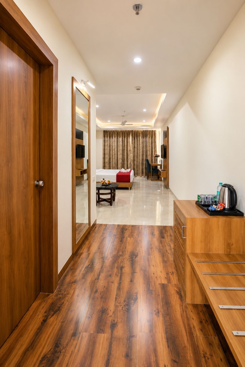 Habitación de hotel con piso de madera, cama con manta roja, escritorio con silla, televisor y estación de café.