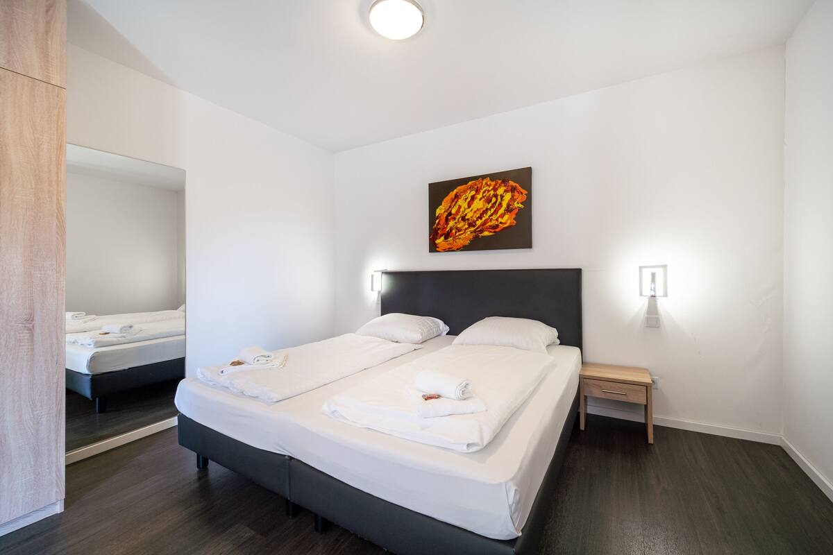 Een hotelkamer met twee bedden, een houten nachtkastje, een aan de muur hangend kunstwerk en een spiegel.