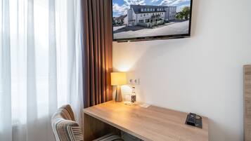 A hotel room with a wooden desk, a chair, a lamp, a bottle, and a remote control.