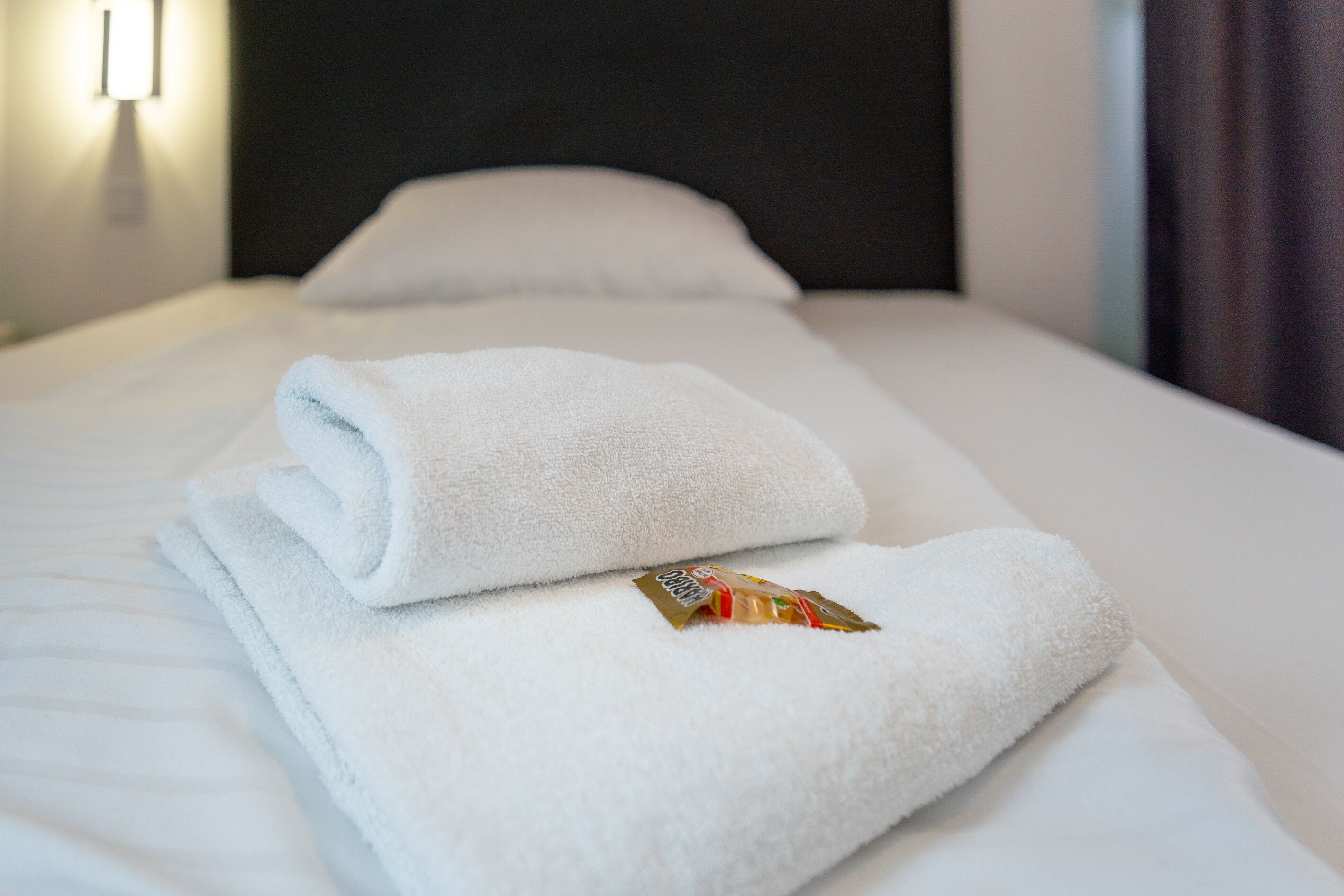 A neatly made bed with white linens and a folded towel with a small item on it.