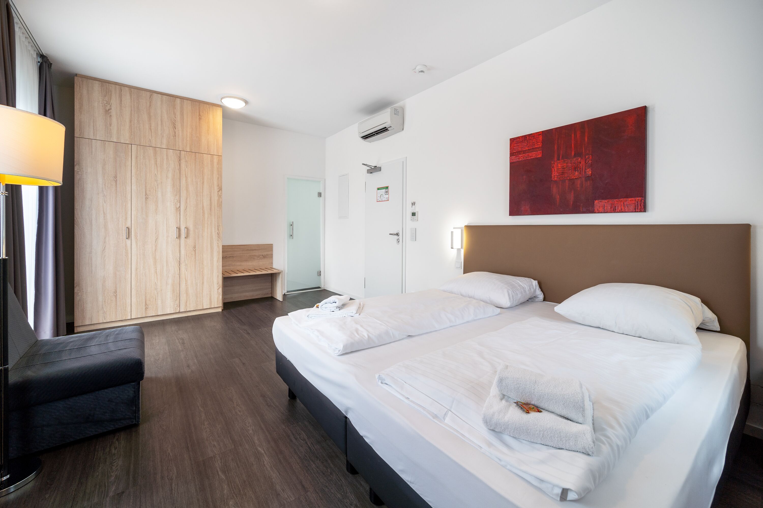 Een hotelkamer met een groot bed, een houten garderobe, een bureau en een modern kunstwerk aan de muur.